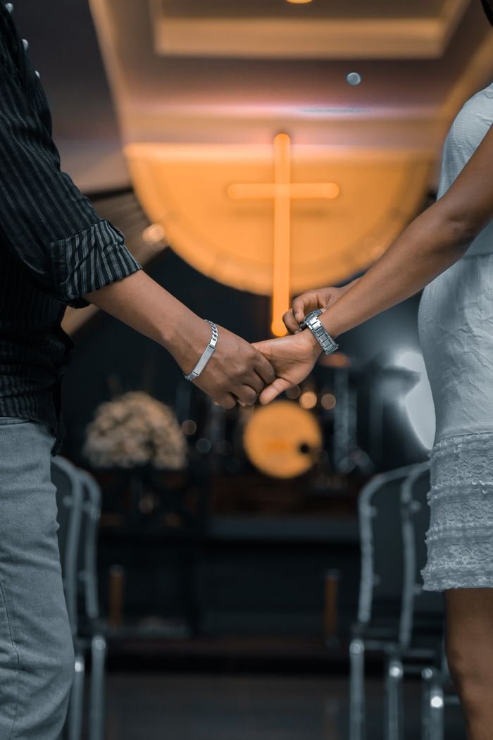 A loving couple holding hands inside a church with a cross in the background.