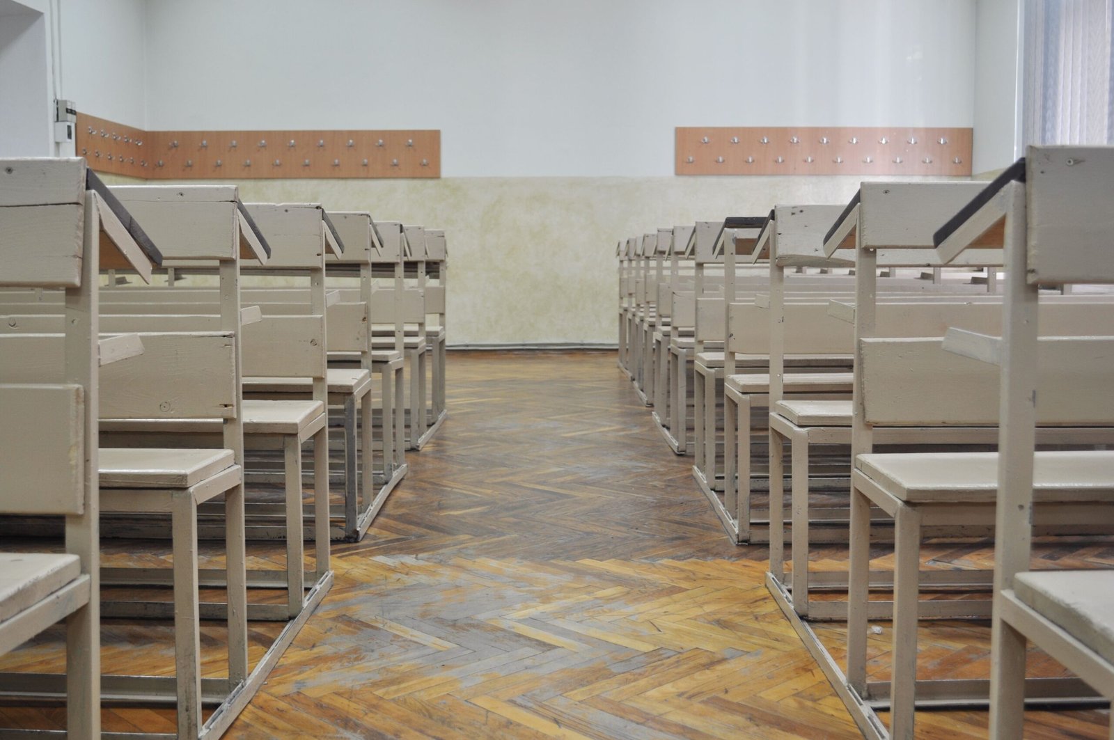 Vintage classroom interior with rows of wooden benches and parquet flooring, evoking a retro academic atmosphere.